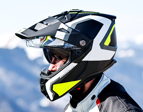 Caberg Tanami Scram helmet in yellow, white, and black color scheme, worn by a man with a mountain landscape in the background.