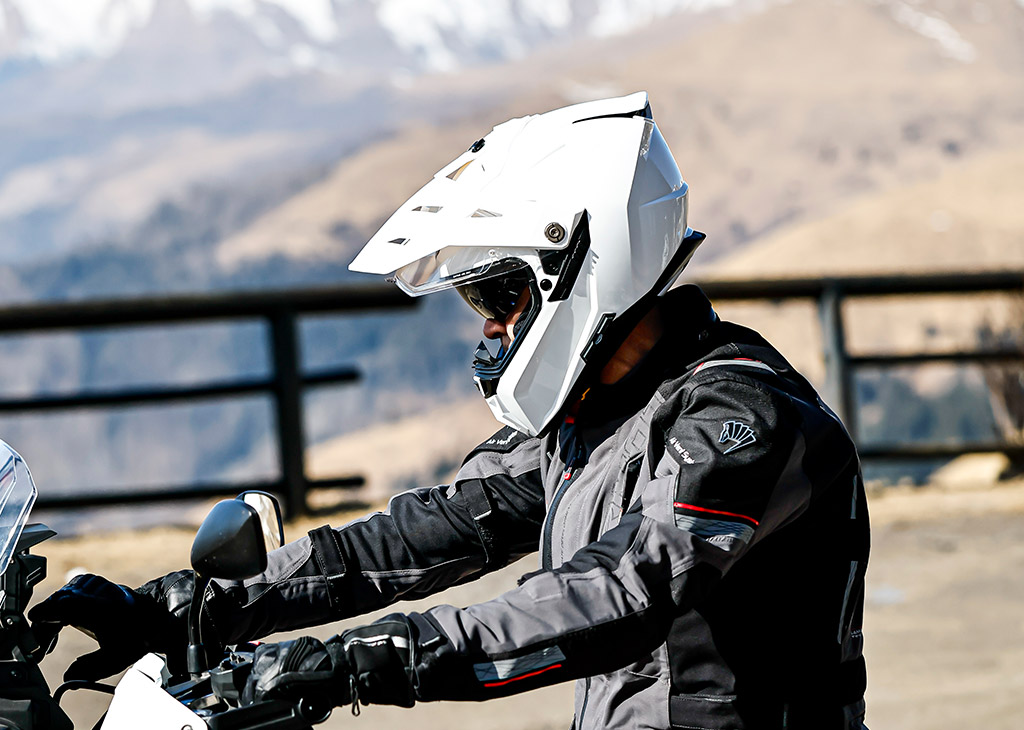 Caberg Tanami helmet in white color, worn by a man riding his motorcycle with a mountain landscape in the background.