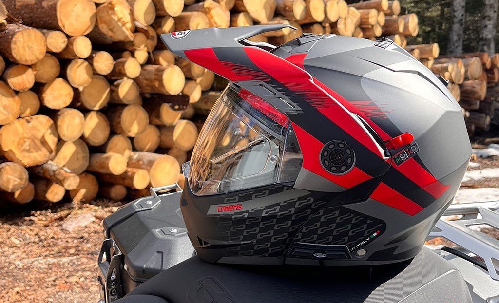 Tourmax X helmet with Bluetooth intercom resting on the motorcycle seat. In the background, chopped wood