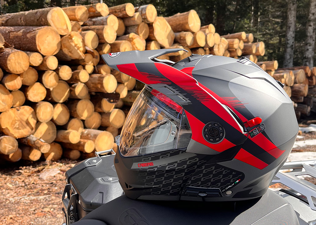 casco Tourmax X con interfono Bluetooth appoggiato sulla sella della moto. Sullo sfondo, della legna tagliata