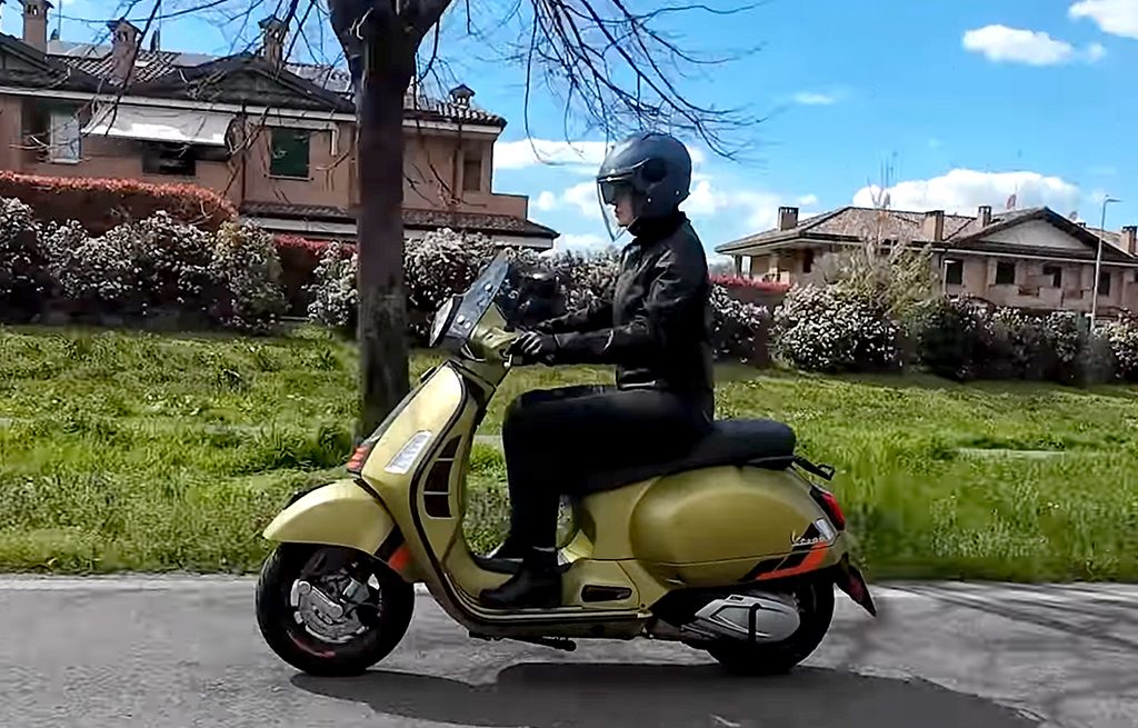 ragazza in sella a una Vespa gialla indossando un casco jet SOHO di colore blu