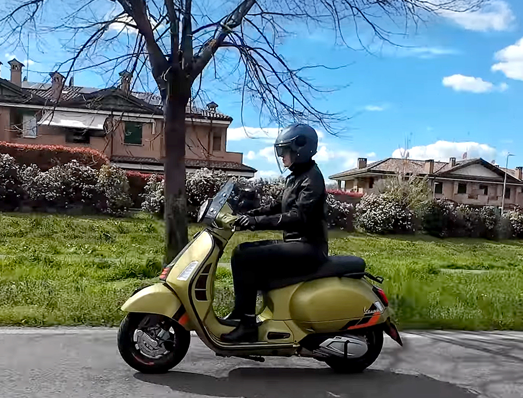 ragazza in sella a una Vespa gialla indossando un casco jet SOHO di colore blu