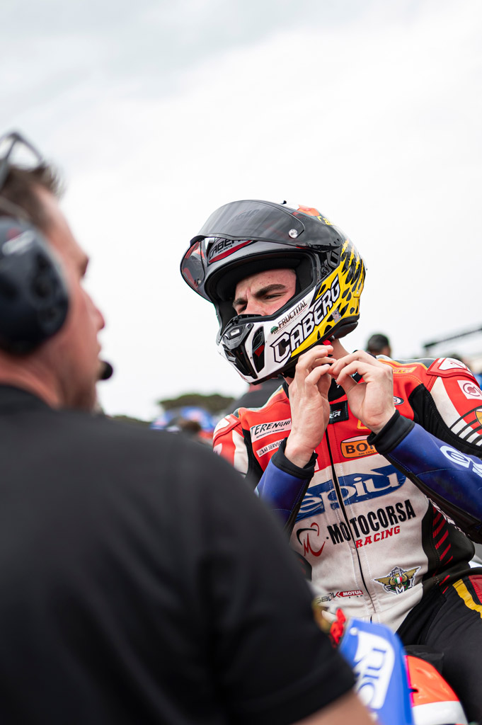 Pilota con casco Caberg GP01 Carbon omologato FIM Level 2 mentre si prepara nel paddock prima della gara