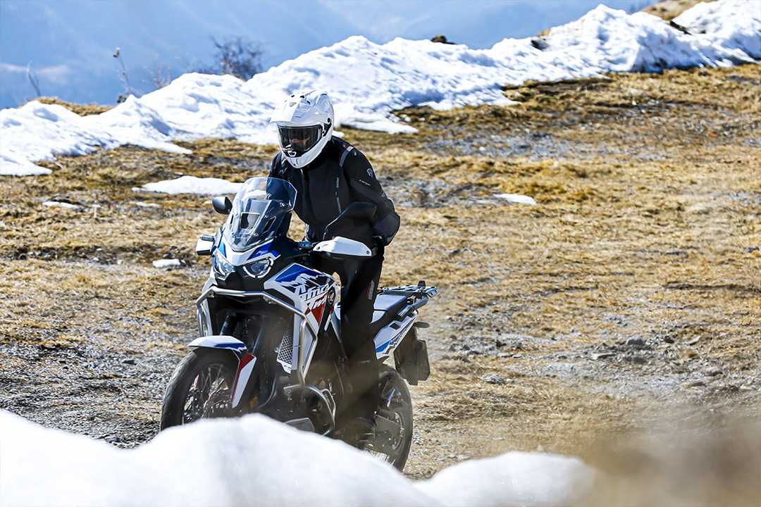 Man on a motorbike in the mountain, wearing Caberg's TANAMI White
